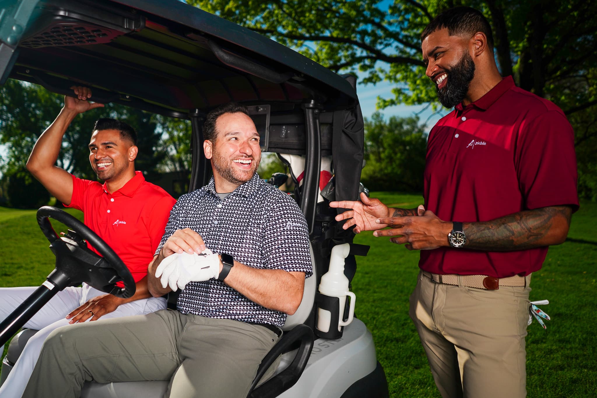 Three golfers in Pichón polos laughing together by a golf cart