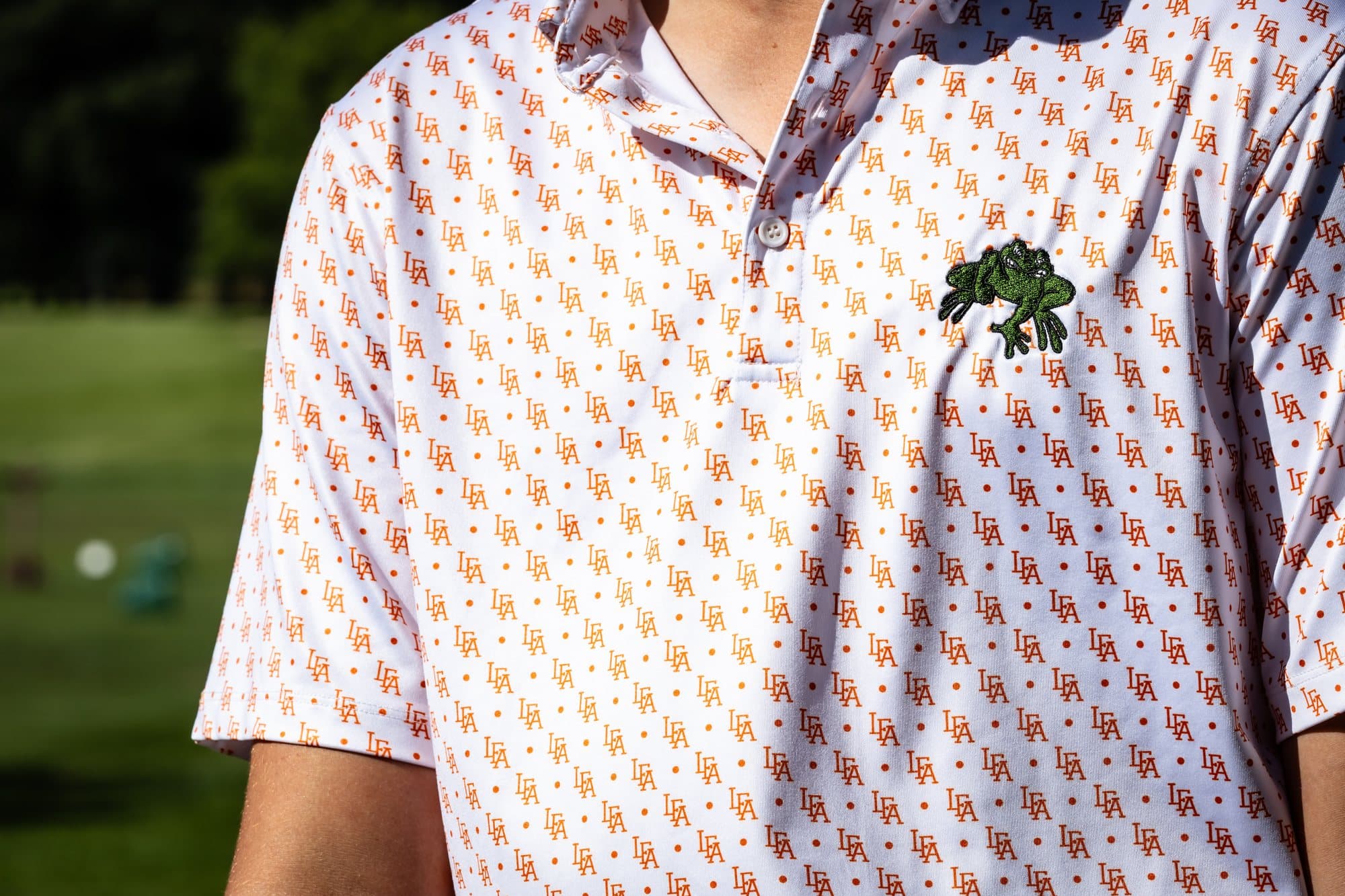 Close-up of a Lake Forest Academy polo with an all-over LFA print and an embroidered frog